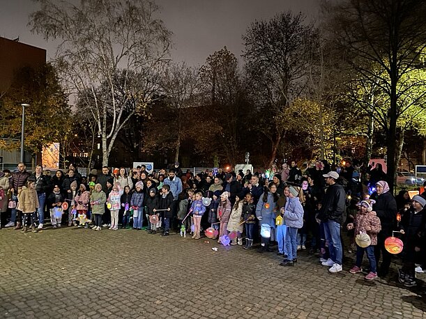Kinder und Eltern mit Laternen singen abends vor dem Haupteingang der Schule