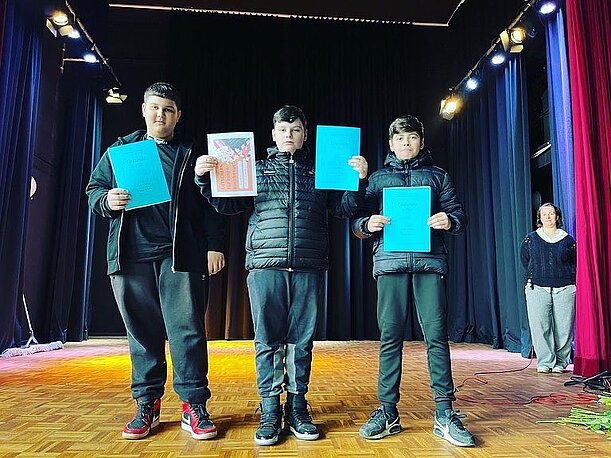Gewinnertrio Blerton, Emir und Mucki aus Klasse 7d mit Urkunden auf der Bühne