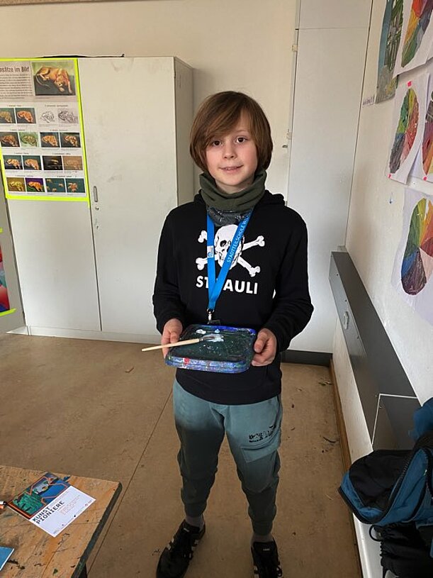 Jakob hält sein Bild „Kanal unter Schnee“ und Malkasten in den Händen