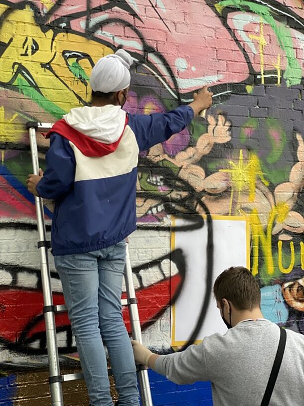 Jugendlicher auf Leiter sprüht Graffiti an eine bunte Wand