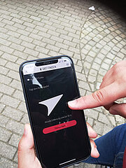 Finger tippt auf Smartphone mit Actionbound-Navigationspfeil
