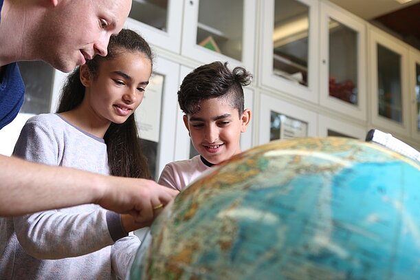 Lehrer erklärt zwei Kindern etwas am Globus