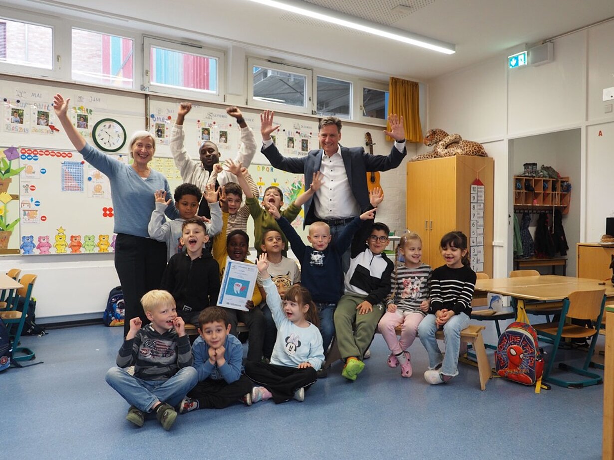 Jubelnde Vorschulklasse mit Lehrkräften im Klassenzimmer nach dem Wettbewerbsgewinn
