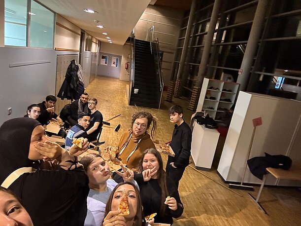 Schülerinnen und Schüler essen Pizza im Flur bei der Halloween-Party