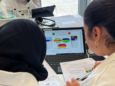 Schülerinnen in Laborkitteln werten Messdaten am Laptop aus