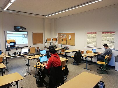 Schülerinnen und Schüler an Laptops im Klassenraum mit Smartboard