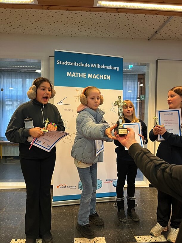 Preisträgerinnen mit Pokal vor dem Roll-up „Mathe machen“