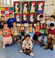 Grundschulkinder mit gebastelten Osterbildern vor gemalten Hähnen