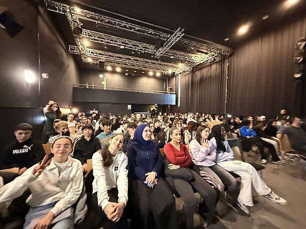 Schülerinnen und Schüler sitzen dicht gedrängt im Publikum der Aula
