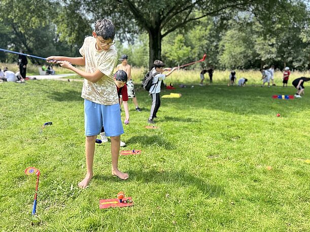 Schüler spielt auf der Wiese ein Wurfspiel mit Stäben