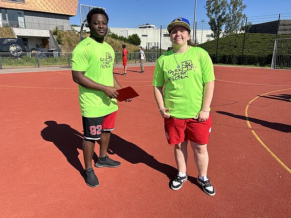 Zwei Parksportpilot:innen in grünen Shirts auf dem Sportplatz