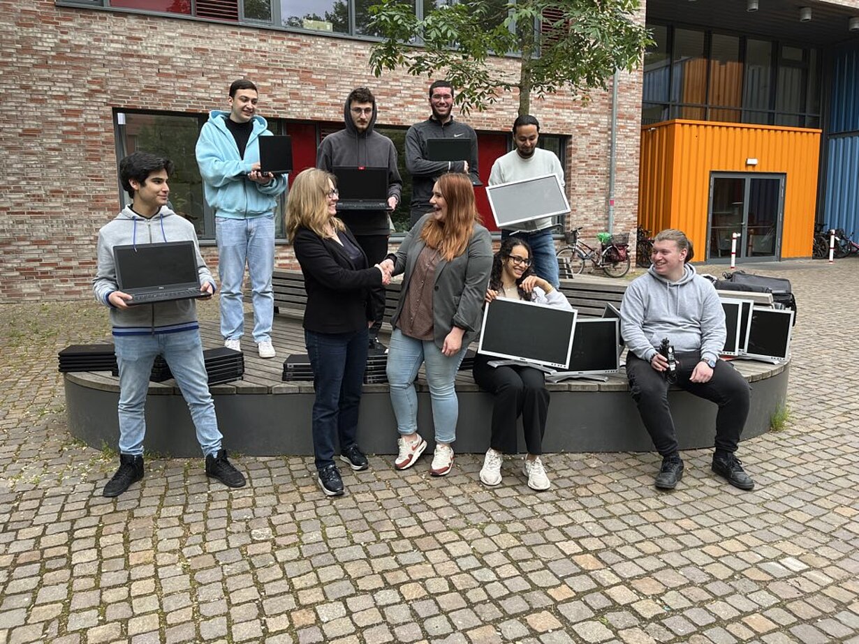 Jugendliche und Erwachsene mit gespendeten Laptops vor dem Schulgebäude