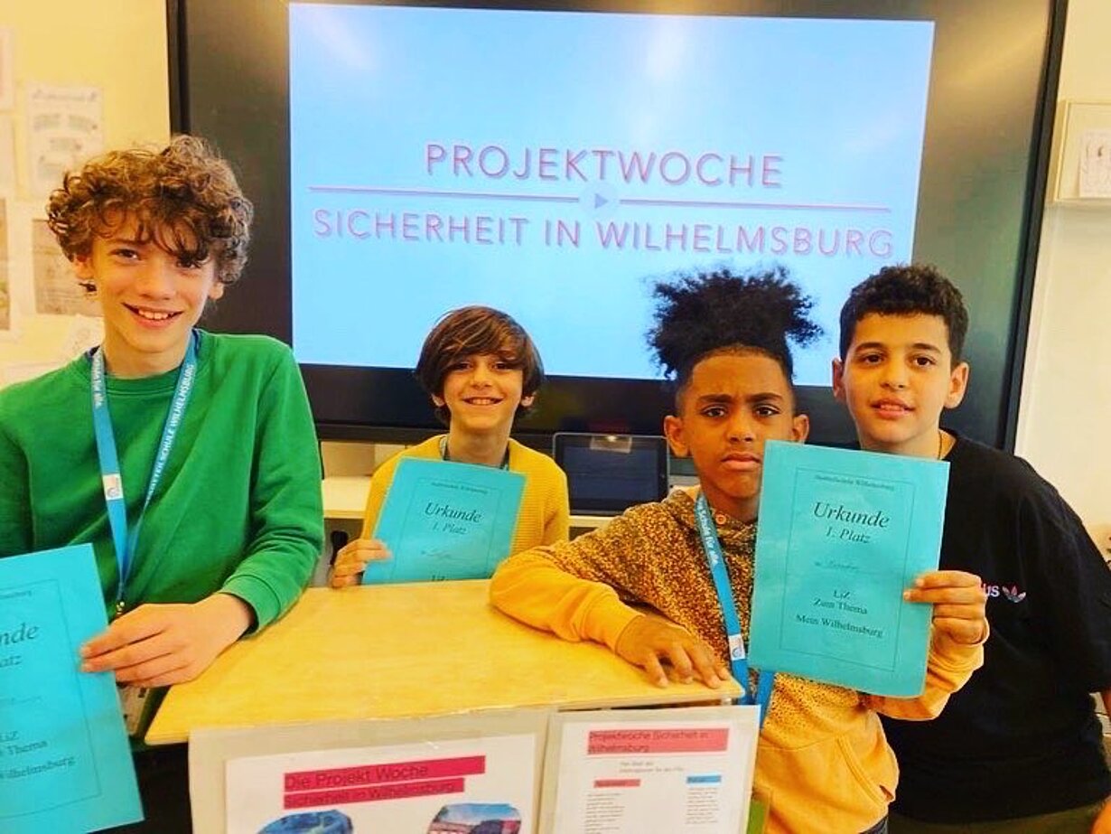 Vier Schüler mit Urkunden vor Leinwand Projektwoche Sicherheit in Wilhelmsburg