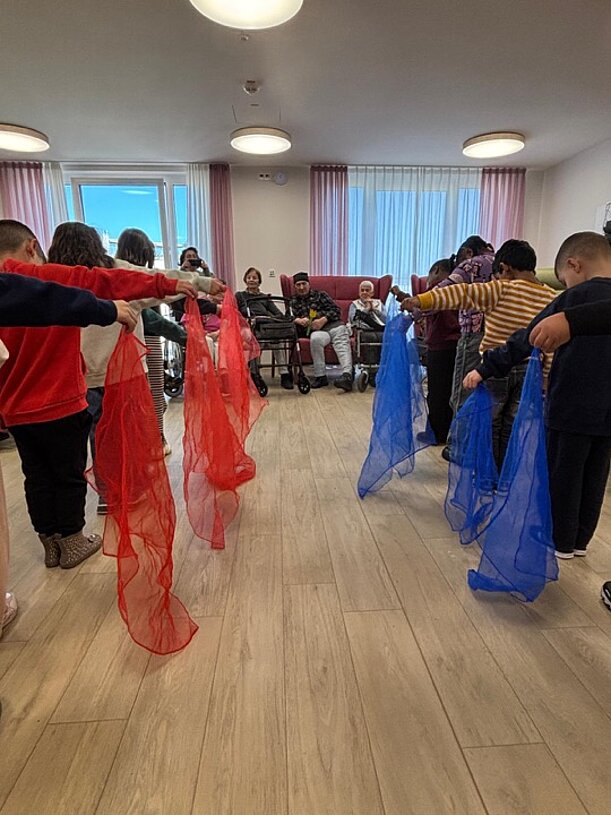 Kinder tanzen mit roten und blauen Tüchern im Gemeinschaftsraum