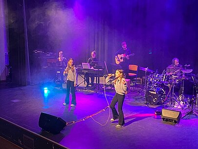 Zwei Sängerinnen und Live-Band auf violett beleuchteter Bühne