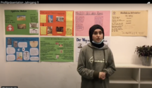 Schülerin präsentiert vor bunten Plakaten an der Klassenzimmerwand