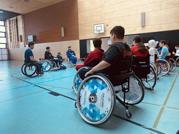 Jugendliche in Rollstühlen im Sitzkreis beim Austausch in der Sporthalle
