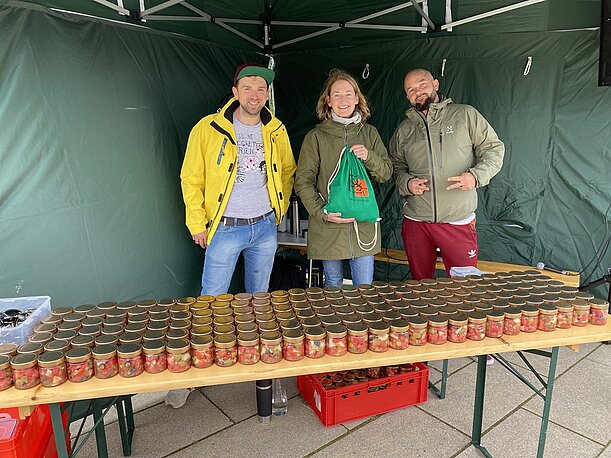 Drei Betreuer am Stand mit Snackgläsern unter einem Zeltdach