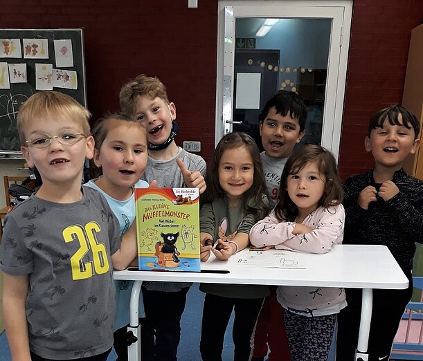 Vorschulkinder mit Bilderbuch um einen Tisch im Klassenraum
