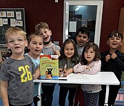 Vorschulkinder mit Bilderbuch um einen Tisch im Klassenraum