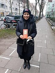 Schülerin mit Mütze hält einen Brief auf einem Gehweg