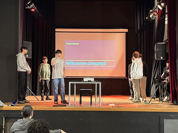 Bühne mit Leinwand „Willkommen Jahrgang 9“ und präsentierenden Schülern