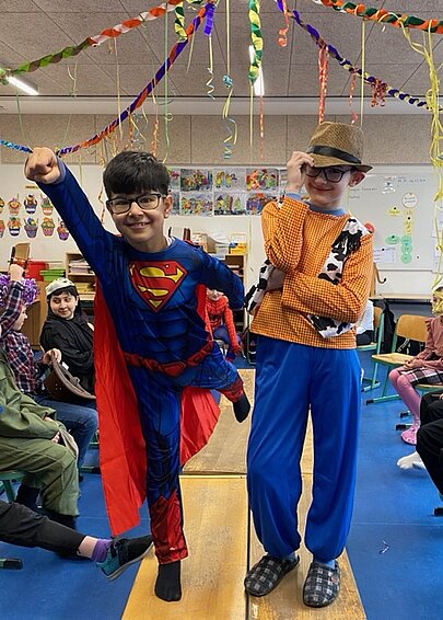 Kinder in Superman- und Cowboykostüm im geschmückten Klassenraum beim Fasching