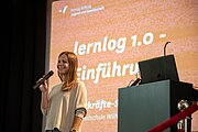 Referentin mit Mikrofon vor Leinwand „lernlog 1.0 – Einführung“