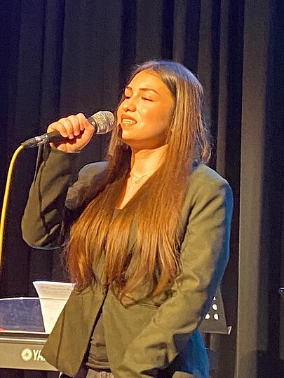 Sängerin mit langen Haaren und Blazer singt mit geschlossenen Augen