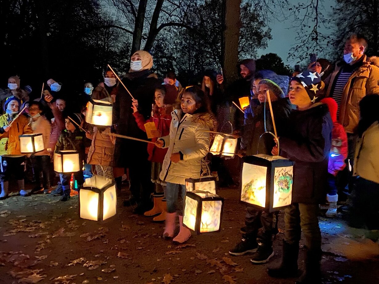 Kinder mit leuchtenden Laternen beim Laternenlauf der Grundschule in der Dämmerung