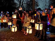 Kinder mit leuchtenden Laternen beim Laternenlauf der Grundschule in der Dämmerung