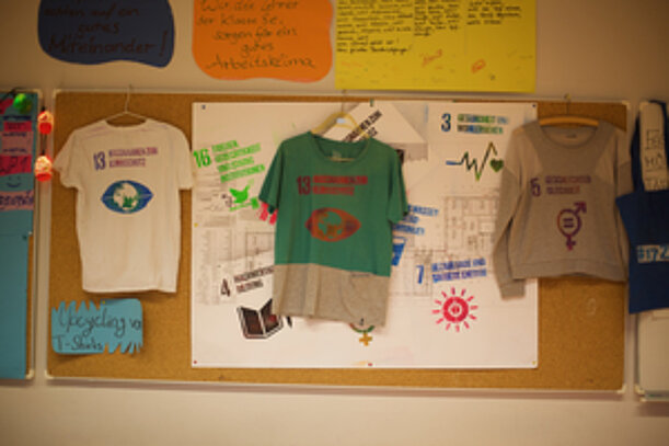 Upcycling-T-Shirts mit Motiven der Nachhaltigkeitsziele an einer Pinnwand