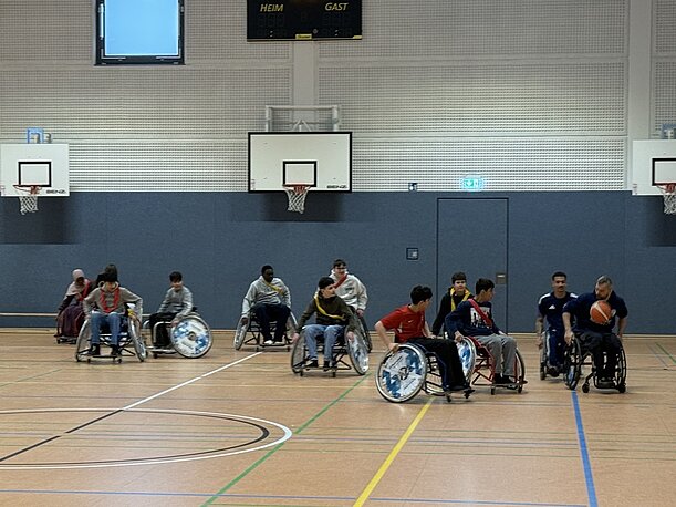 Schülerinnen und Schüler rollen in Sportrollstühlen über das Hallenfeld