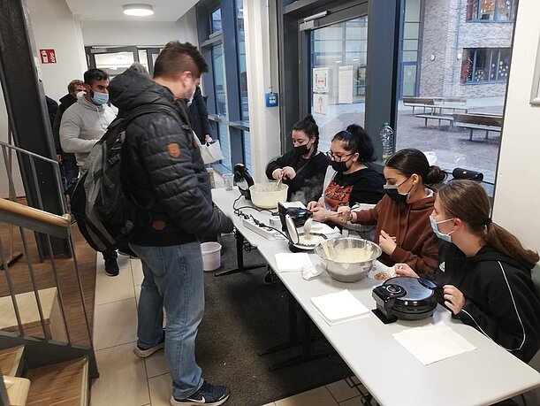 Schülerinnen backen Waffeln an einem Tisch im Treppenhaus