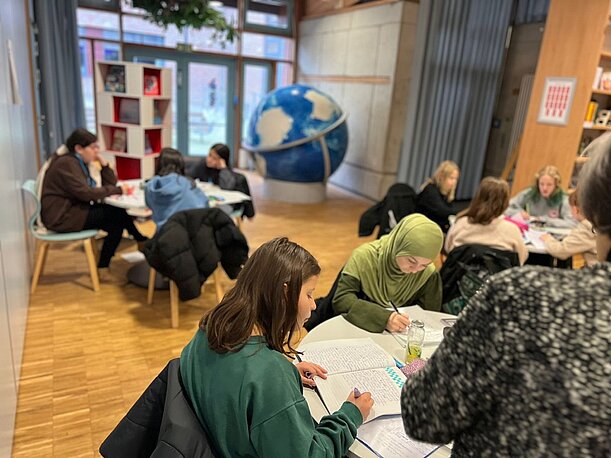Schülerinnen und Schüler schreiben konzentriert an Tischen in der Bibliothek