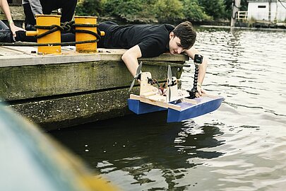 Schüler setzt vom Steg aus ein ferngesteuertes Modellboot ins Wasser