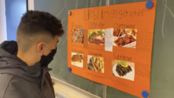 Schüler betrachtet ein orangefarbenes Plakat Lieblingsgerichte mit Essensfotos
