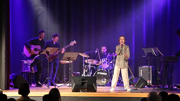 Junge Sängerin in Karojacke singt mit Band beim The Voice of Wilhelmsburg