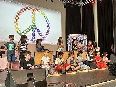 Klasse 2c musiziert auf der Bühne vor Leinwand mit Peace-Zeichen