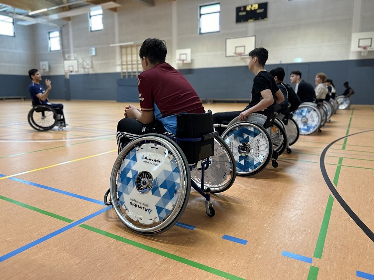 Jugendliche in Sportrollstühlen reihen sich in der Sporthalle auf
