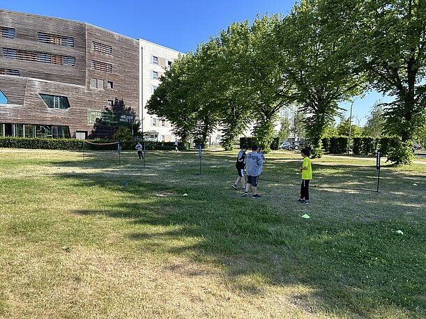 Kinder spielen auf einer Wiese vor Wohngebäuden beim Sporttag