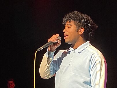 Nahaufnahme eines Sängers mit Locken in hellblauer Jacke