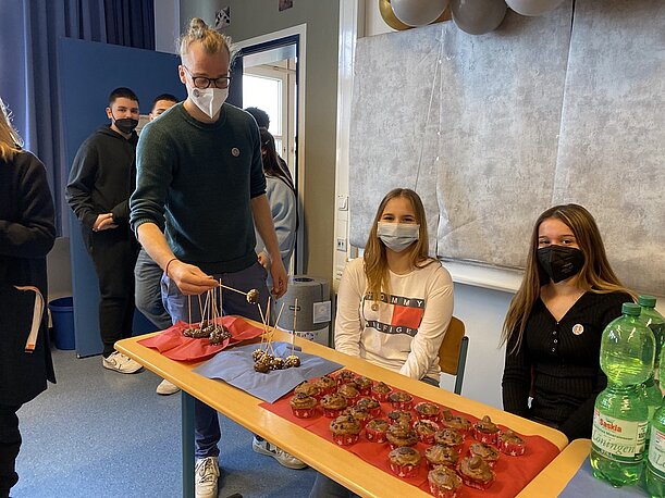 Schülerinnen und Lehrer am Tisch mit Kuchen und Getränken