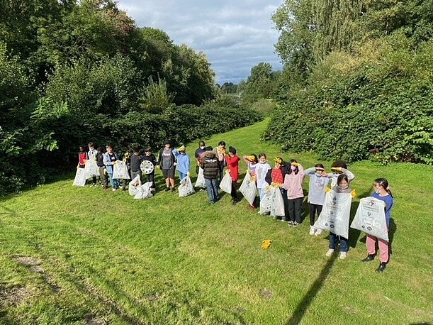 Lange Reihe Kinder mit vollen Müllsäcken auf einer Wiese beim Aufräumen