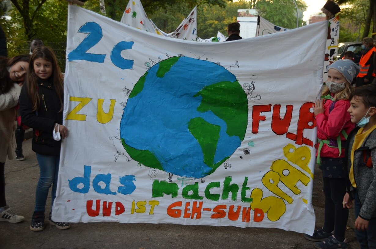 Kinder mit Transparent „2c zu Fuß – das macht Spaß“ und Erdball