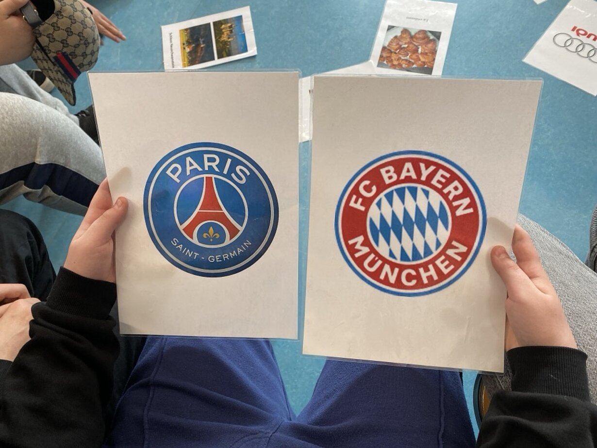 Hände halten Karten mit Logos von Paris Saint-Germain und FC Bayern München