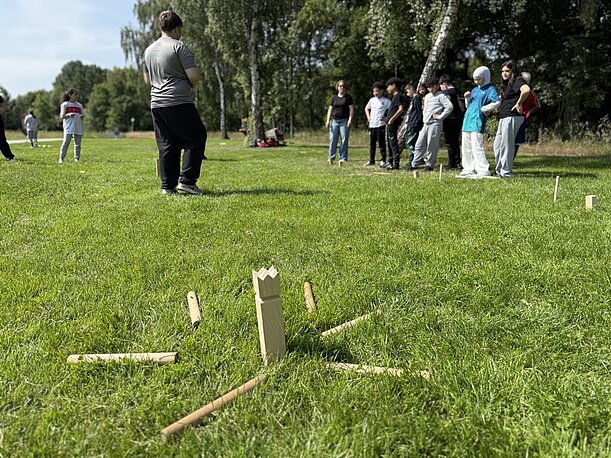Kubb-Spiel auf der Wiese, im Hintergrund Jugendliche