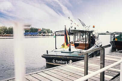 Kleines Schiff mit Deutschlandflagge und Aufschrift Hamburg am Anleger