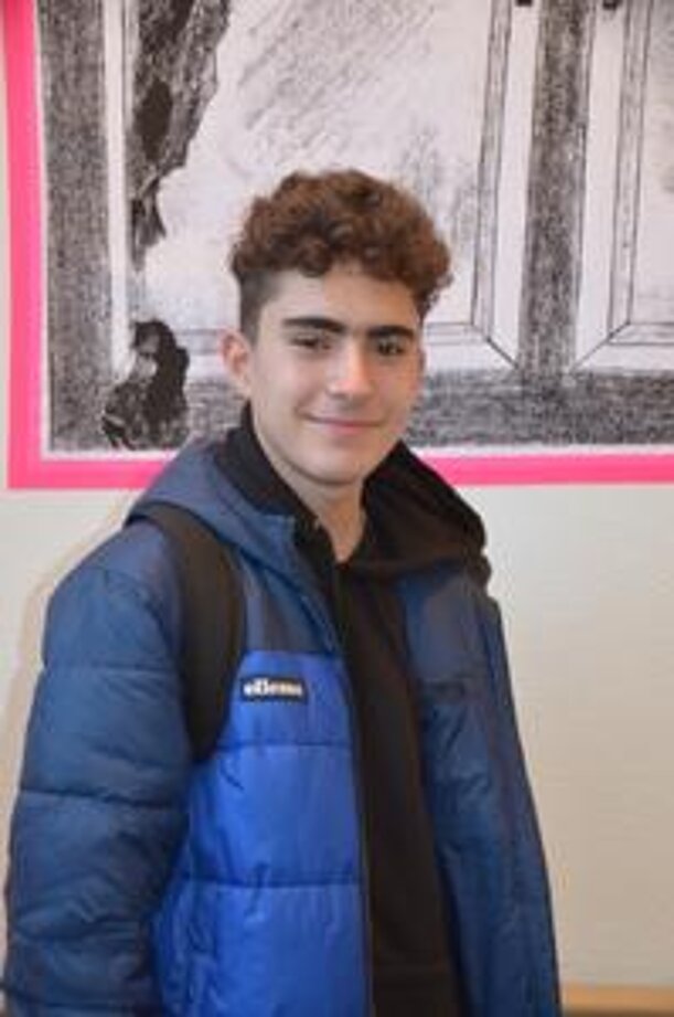 Lächelnder Schüler in blauer Jacke vor einer Zeichnung