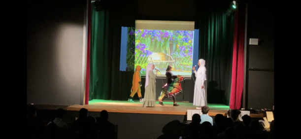 Bunt kostümierte Figuren vor Blumenkulisse beim Theaterstück „Der geheime Garten“